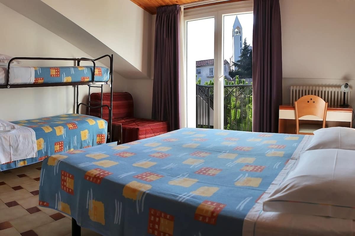 A hotel room with two bunk beds, a desk, a chair, and a view of a building with a tower.