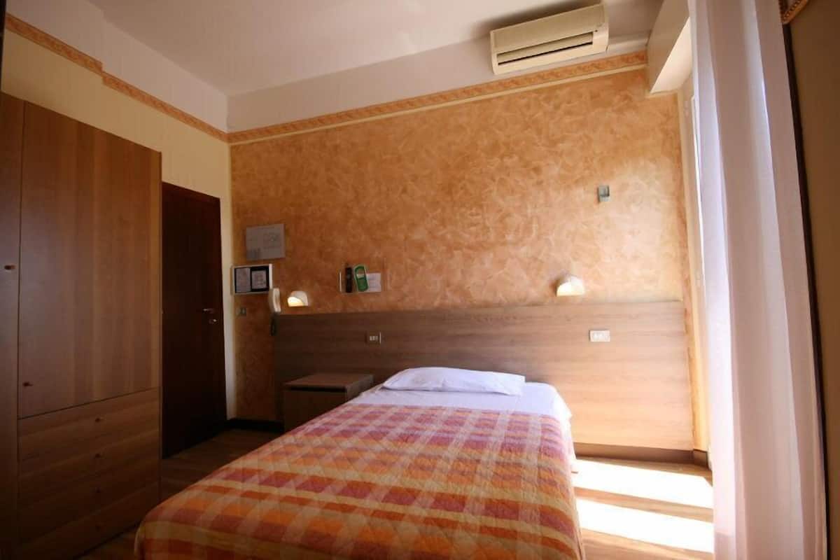 A hotel room with a wooden headboard, a bed with a checkered bedspread, a nightstand, and a wall-mounted air conditioning unit.