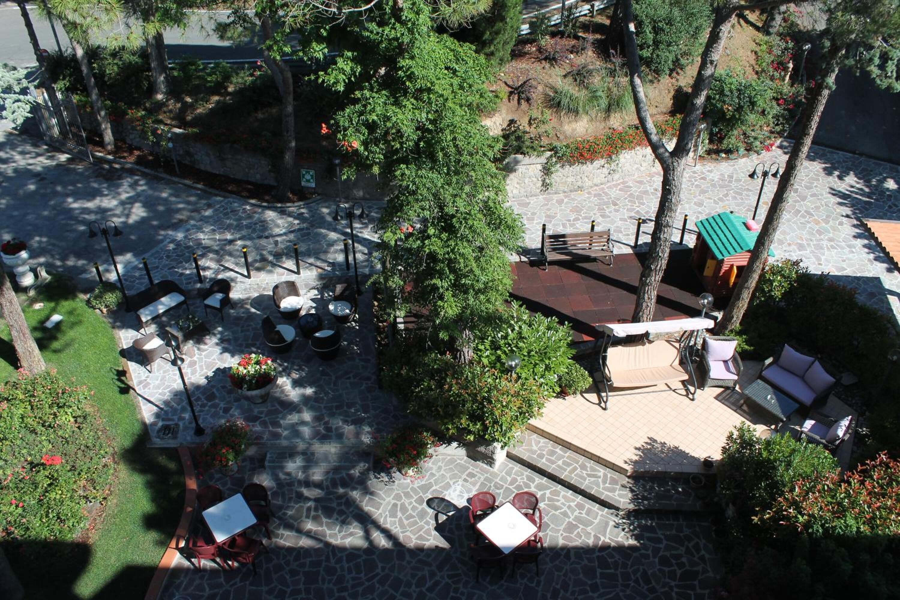 Un espace extérieur aménagé en terrasse, avec un sol en pierre, de nombreux coins salon comprenant des tables et des chaises, le tout entouré de verdure et d’arbres.