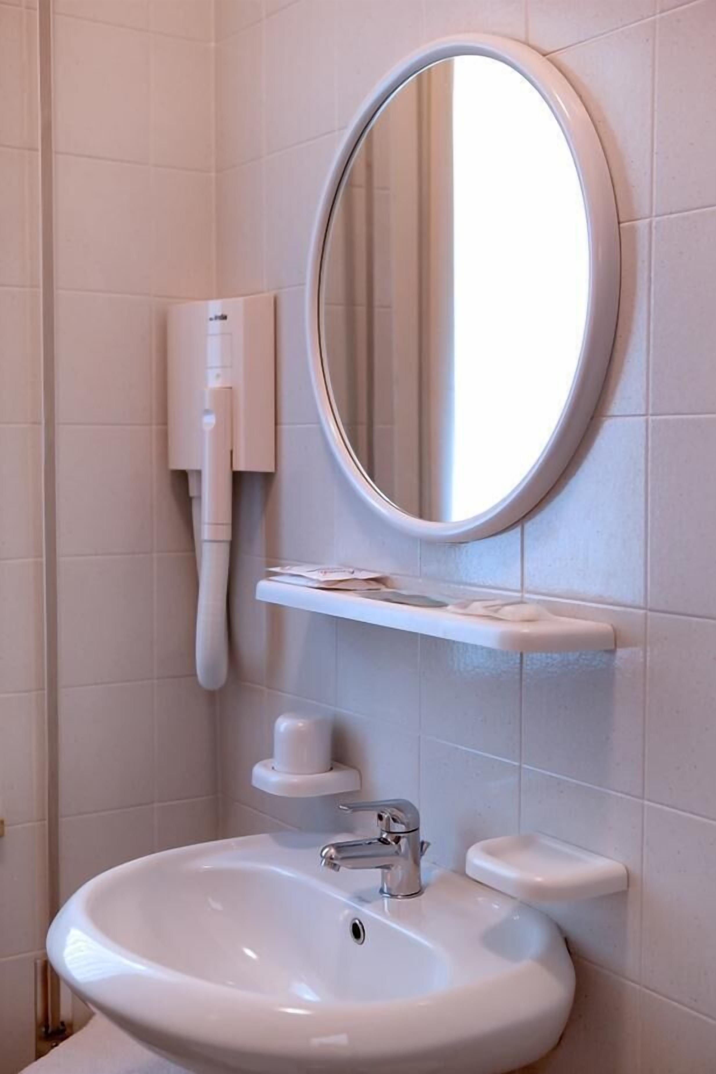 Une salle de bain avec un lavabo blanc, un miroir rond, un distributeur de savon et un porte-serviettes.