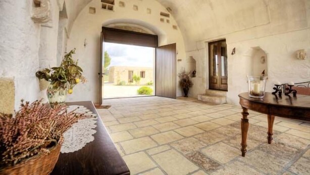 Um interior com soalho de pedra, uma porta em arco e vista para o exterior.