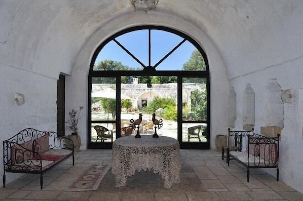 A room with a large arched window, a table with a lace tablecloth, and two metal beds.