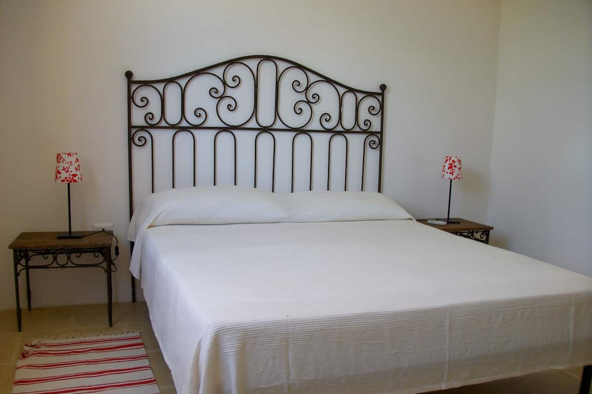 A neatly made bed with a metal headboard, two bedside tables with lamps, and a striped rug on the floor.