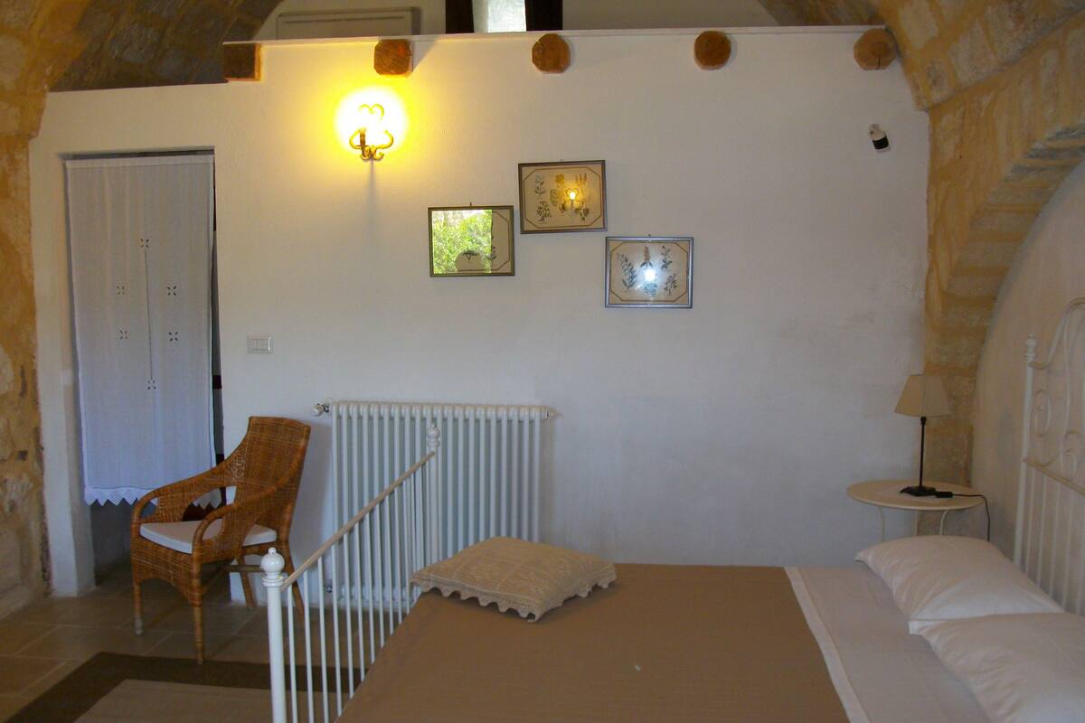 A bedroom with a bed, a chair, a radiator, and a wall with three framed pictures.