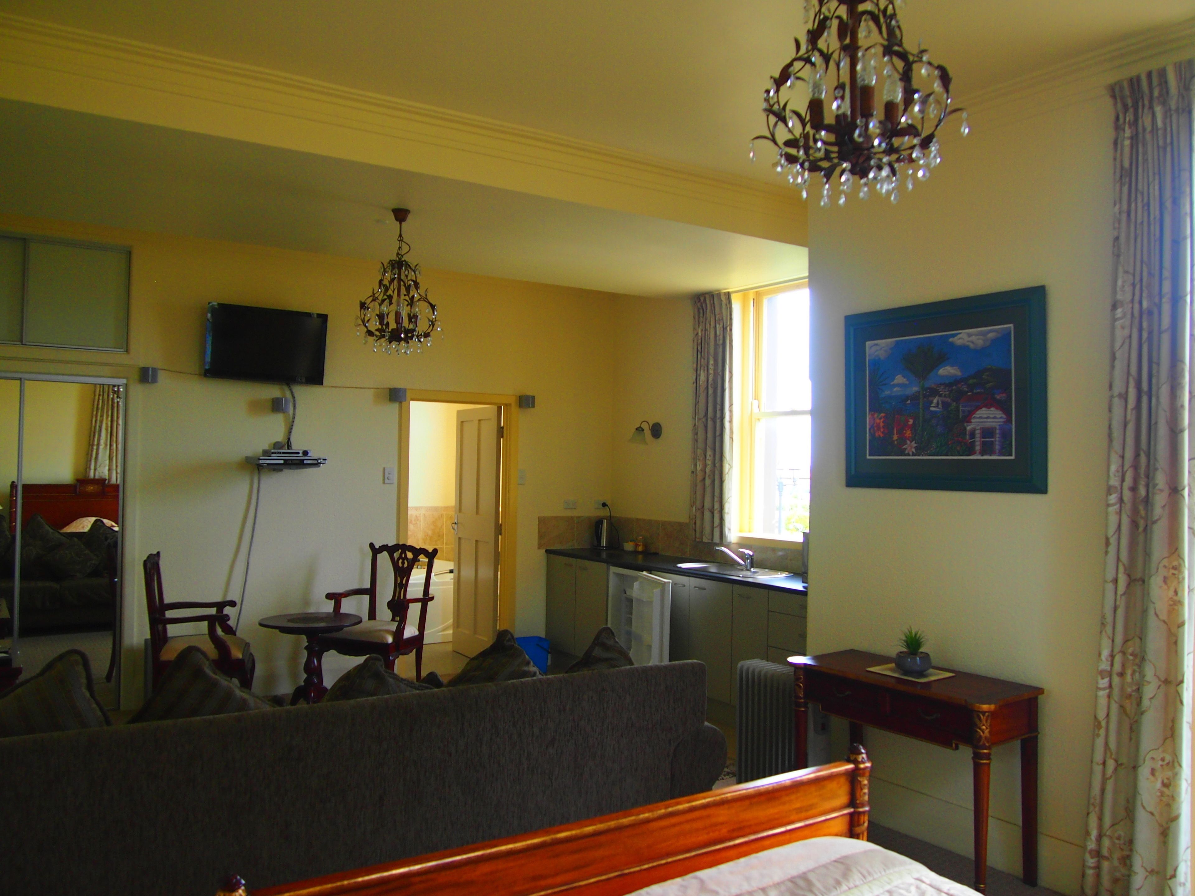 Een hotelkamer met een bed, een zithoek met een stoel en een tafel, een kitchenette, een aan de muur bevestigde televisie en een kroonluchter.