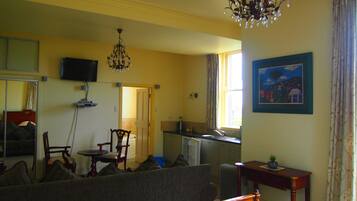 Een hotelkamer met een bed, een zithoek met een stoel en een tafel, een kitchenette, een aan de muur bevestigde televisie en een kroonluchter.