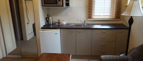 Una cocina compacta equipada con microondas, refrigerador, lavamanos y una pequeña mesa de comedor.