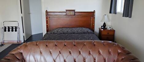 Un dormitorio con un amplio sofá de cuero, una cama de madera con cabecera, una mesita de noche con lámpara y una ventana con cortinas.