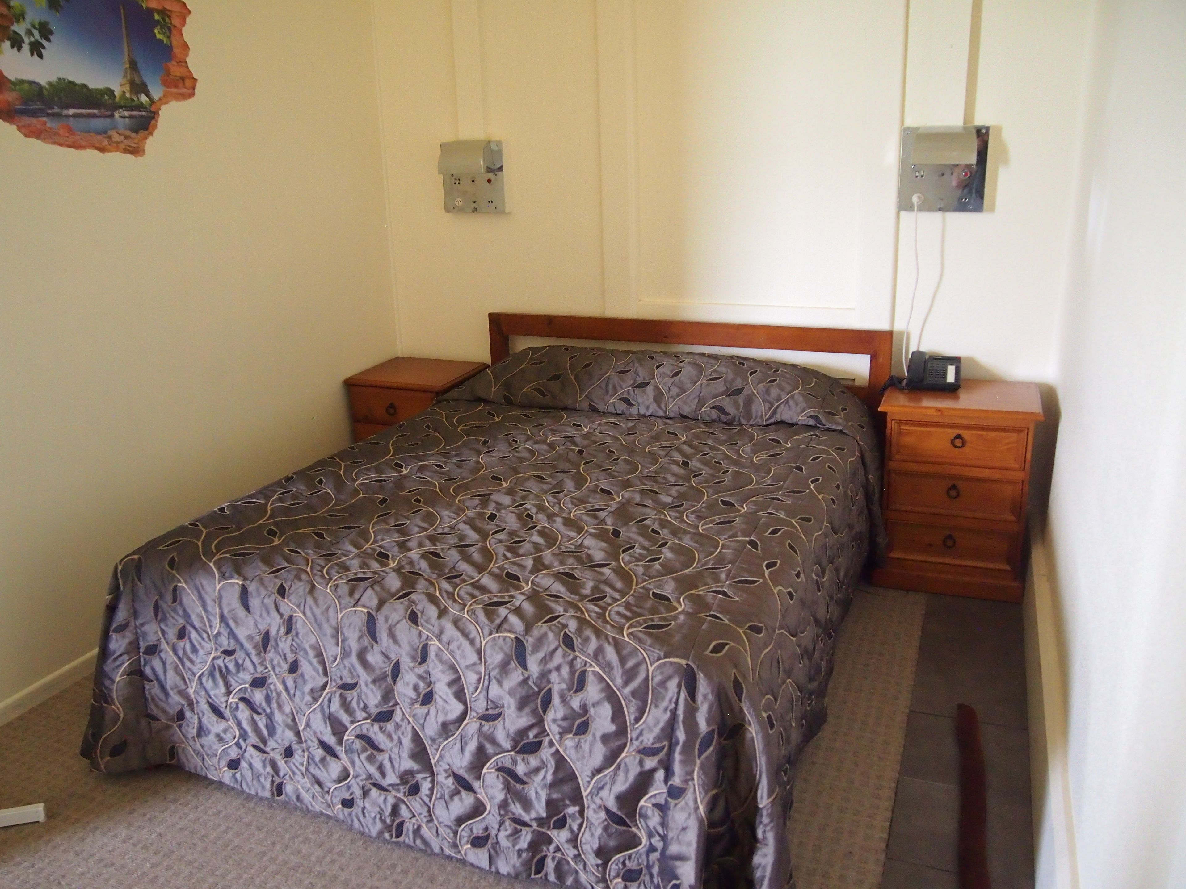 A bedroom with a bed, wooden nightstands, and a wall-mounted electrical outlet.