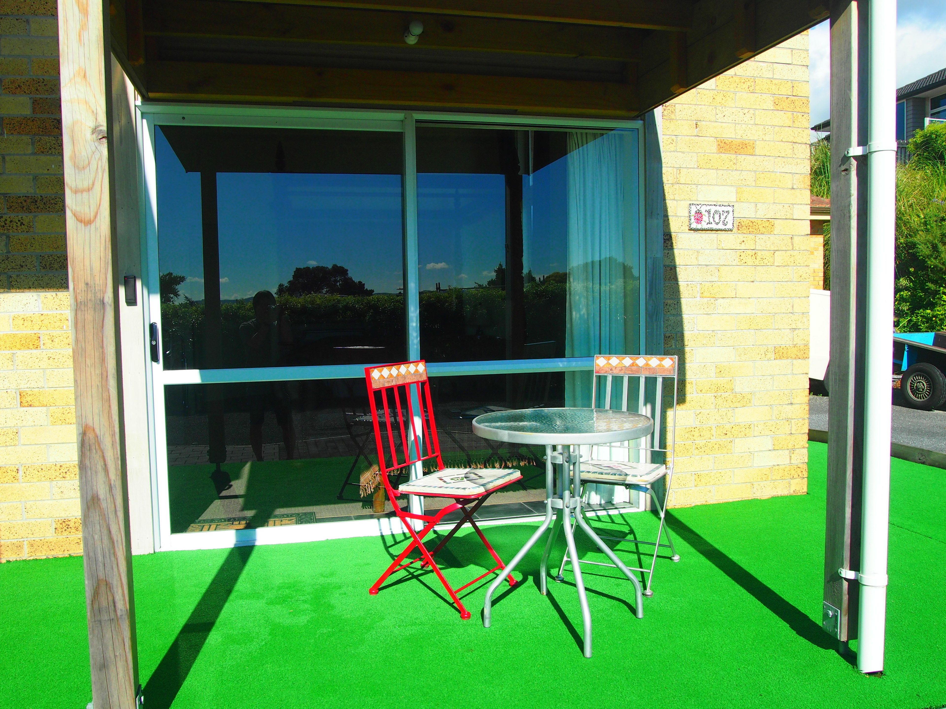 Un espace patio avec une porte vitrée donnant sur un balcon, une chaise pliante rouge et une petite table.