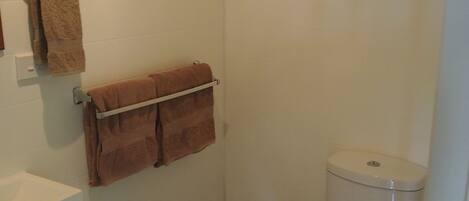 A small, clean bathroom with a toilet, a towel rack with two towels, and a white sink.