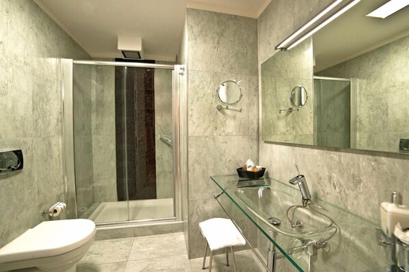 A modern bathroom with a glass shower enclosure, a glass sink, and a large mirror.