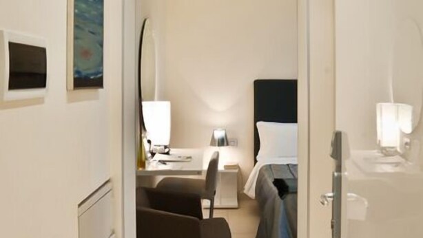 A narrow hallway leading to a bedroom with a bed, bedside table, and a chair. There is a painting on the wall and a mirror above the bed. - Town House Cavour (Reggio Calabria)