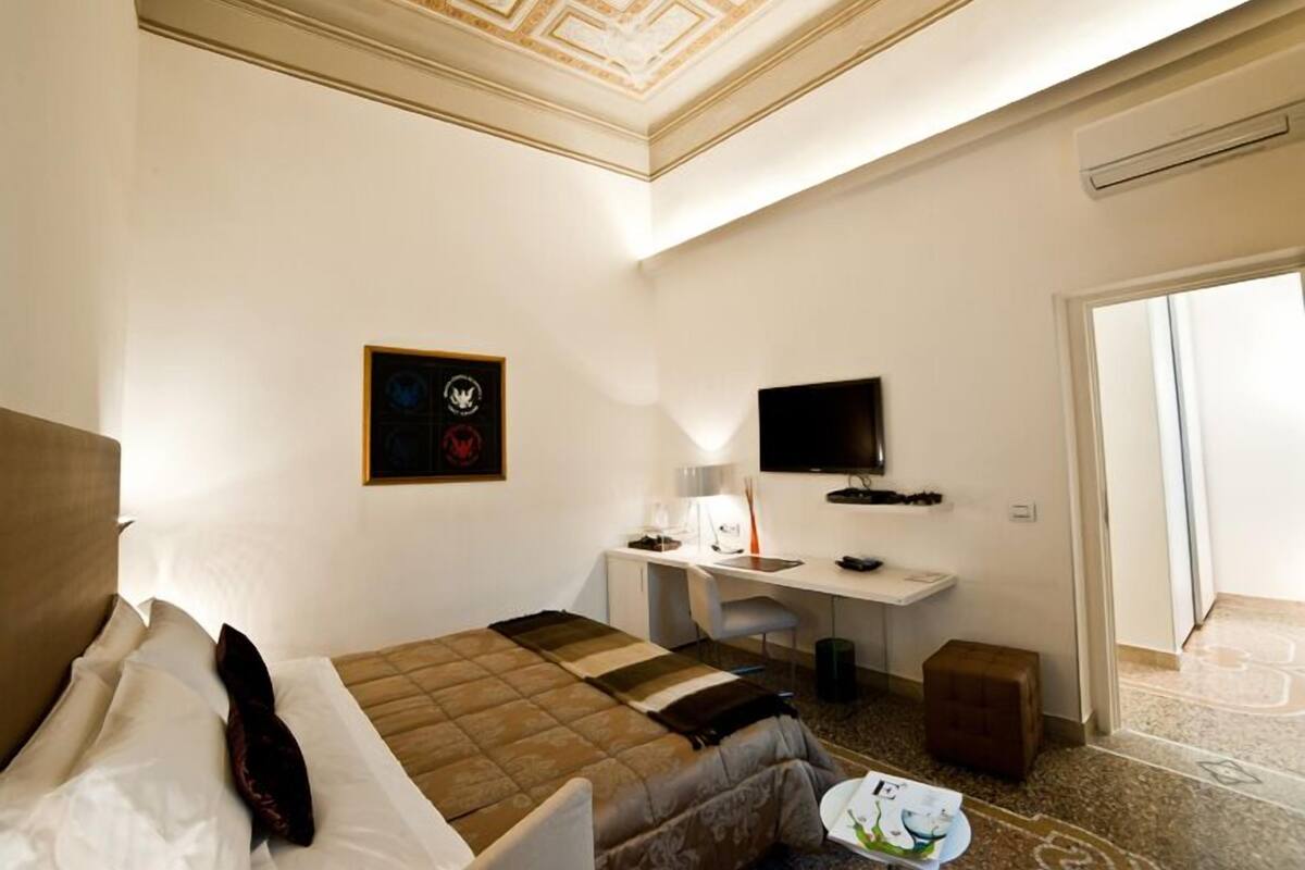 Habitación de hotel con cama, escritorio con computadora, televisor y pequeña mesa con un libro.