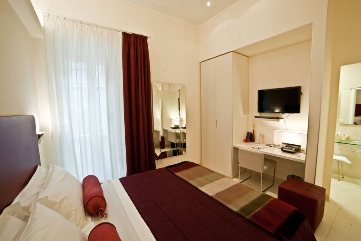 Una habitación de hotel con cama, escritorio, televisor y espejo.