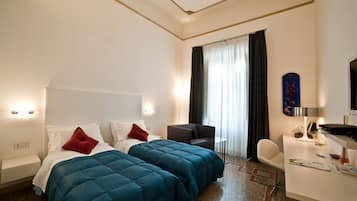 A hotel room with two beds, a desk, a chair, a small table, and a window with curtains.