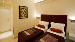 A hotel room with two single beds, a door, a wall-mounted painting, and a nightstand with a lamp. - Town House Cavour (Reggio Calabria)