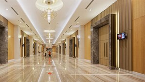 A hotel corridor with a polished marble floor, modern lighting fixtures, and digital screens displaying content. - HARRIS Hotel & Conventions Kelapa Gading Jakarta (Jakarta)