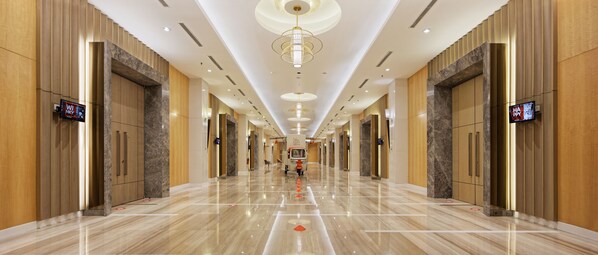 Un pasillo de hotel con piso de mármol pulido, luminarias modernas y pantallas digitales mostrando contenido.