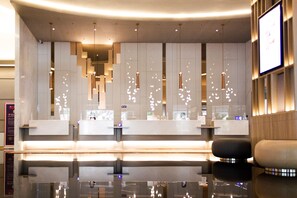 Un área de recepción moderna con un mostrador de vidrio, iluminación colgante y una zona de estar con sofá negro y beige.