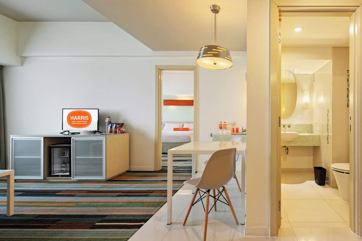 Quarto de hotel com cama, mesa de cabeceira, escrivaninha, cadeira e vista para o banheiro.