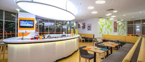 Una cafetería moderna con mostrador central, zona de estar y grandes ventanales.