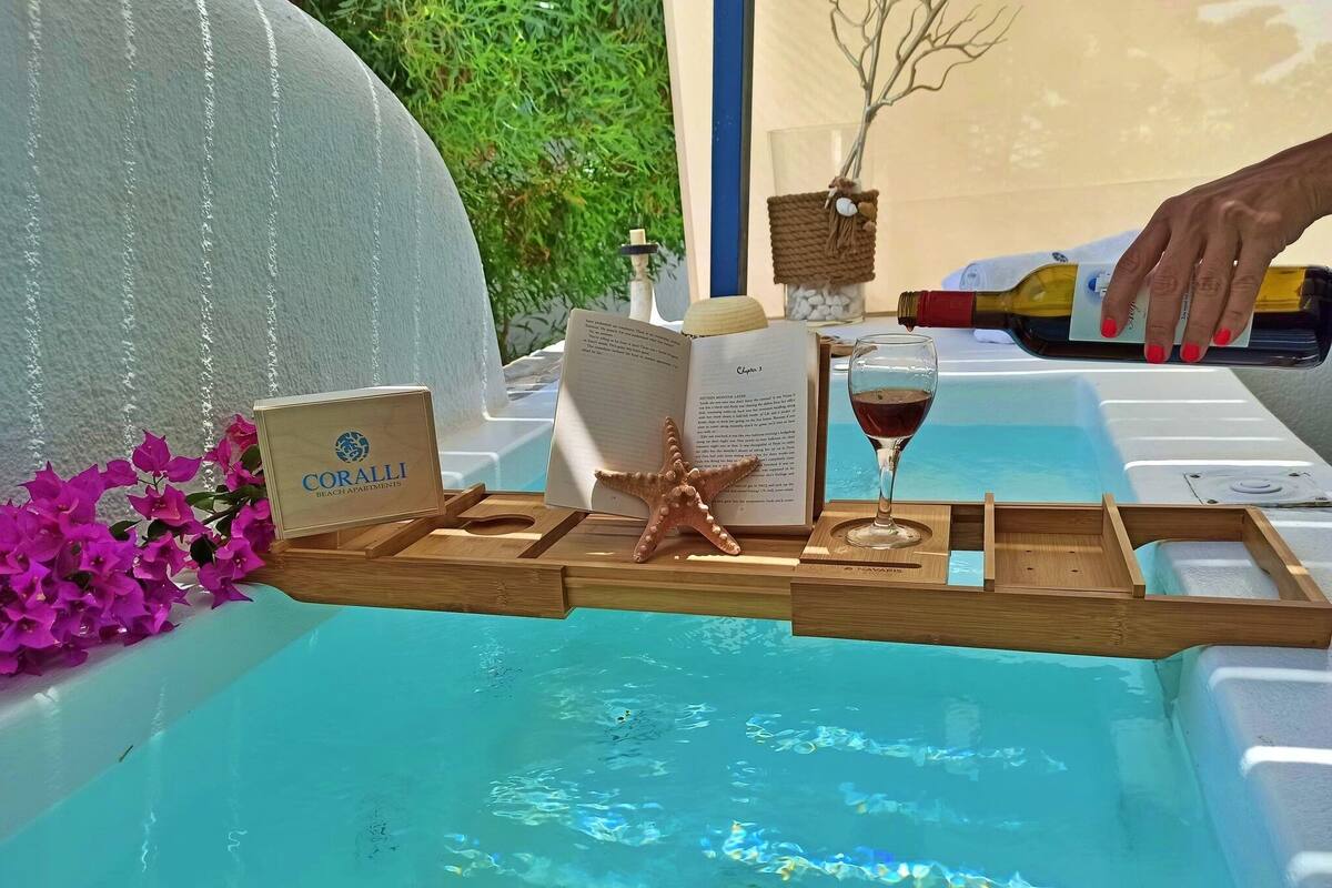 A wooden tray with a book, starfish, and a wine glass on a poolside table.