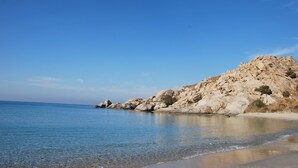 Une plage avec une eau d’un bleu limpide, un terrain rocheux et un ciel dégagé.