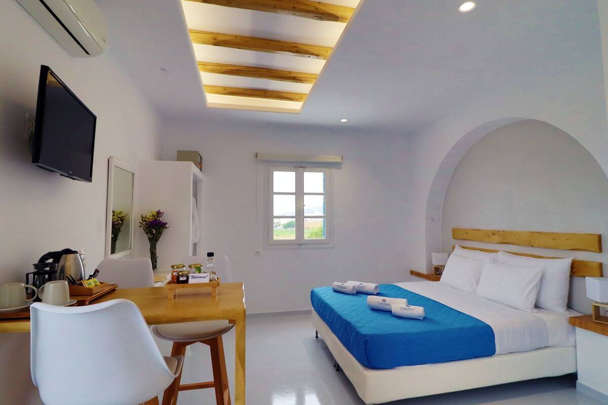 A bedroom with a bed, a desk, a chair, a TV, and a window.