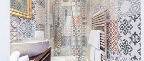 A bathroom with a stone sink, a toilet, a shower, and patterned tiles.