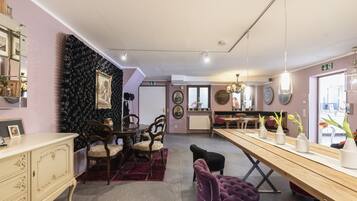 A dining area with a wooden table, chairs, and a purple ottoman. There is a black wall with a textured pattern and a white cabinet with drawers.