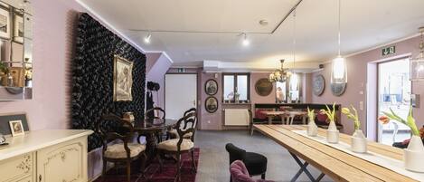 A dining area with a wooden table, chairs, and a purple ottoman. There is a black wall with a textured pattern and a white cabinet with drawers.