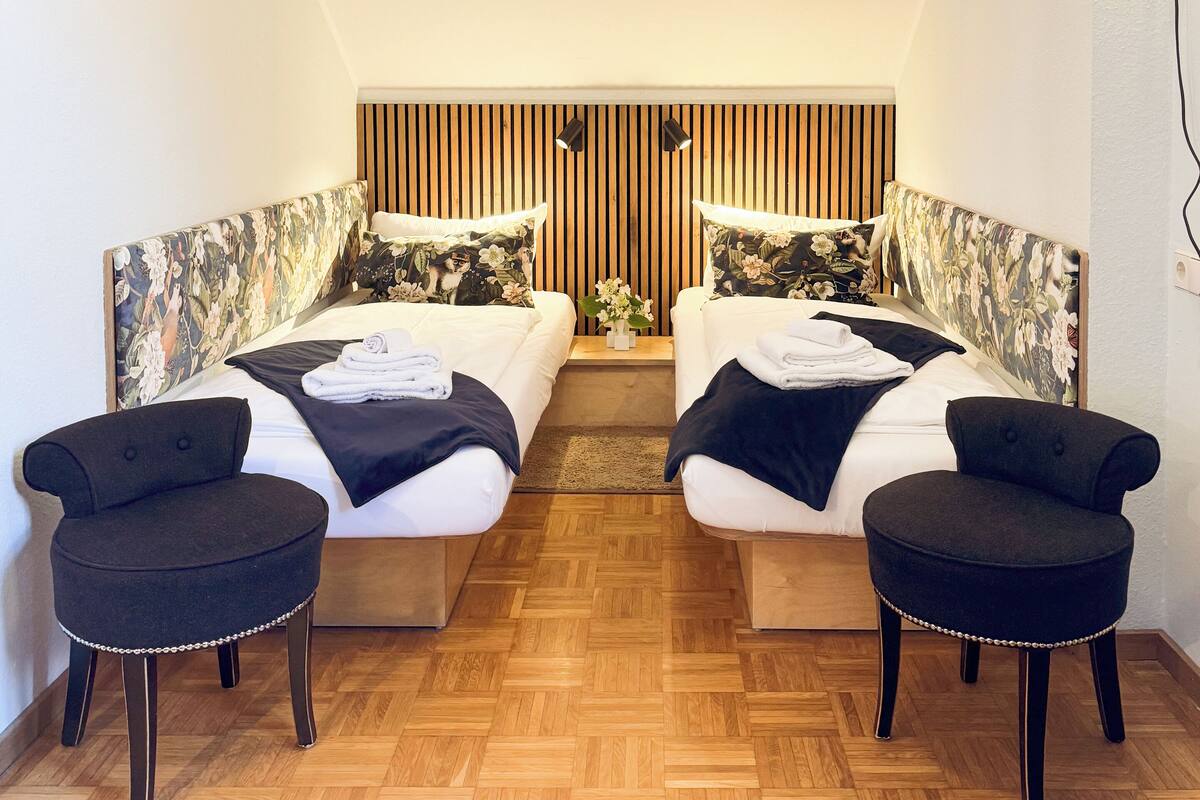 A room with two beds, a wooden floor, and a sloped ceiling.
