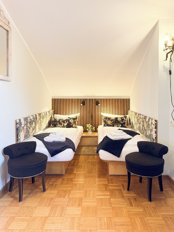 A room with two beds, a wooden floor, and a sloped ceiling. - Villa Fantasia Budget Boutique Hotel (Fuessen)