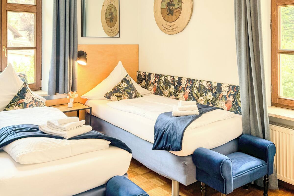 A well-lit bedroom with a bed, two chairs, a nightstand, and a mirror.