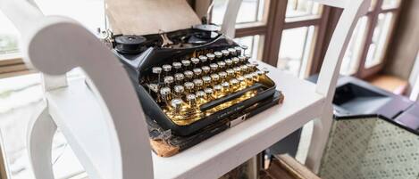 A vintage typewriter on a white chair with a window in the background.