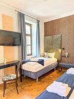 Habitación de hotel con cama, escritorio, silla, televisión y ventana con cortinas.