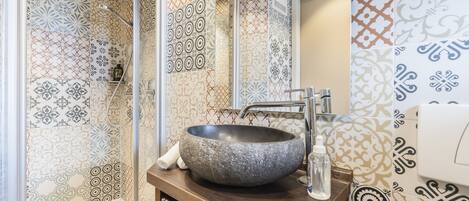 A bathroom with a large stone sink, a glass shower enclosure, and patterned tiles.