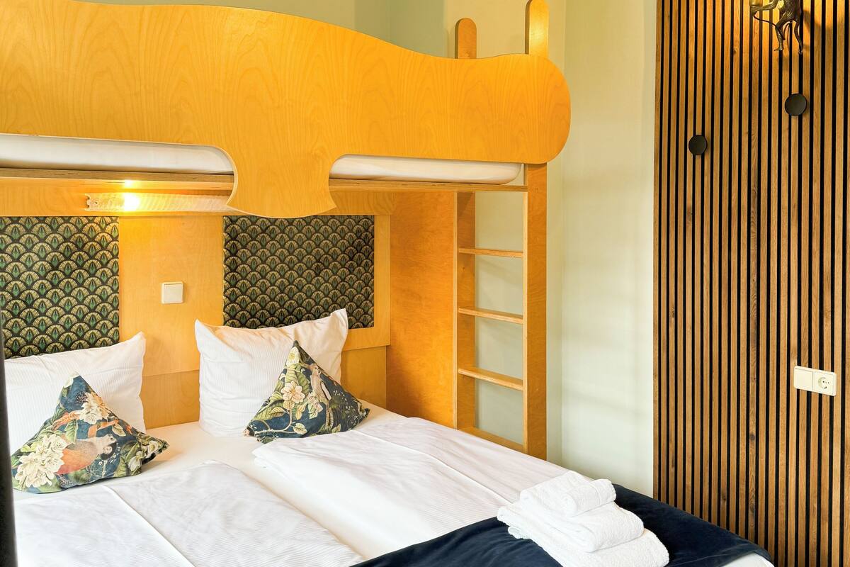 A double bed with white linens and two pillows, a wooden headboard, a ceiling with a textured design, and a wall-mounted light fixture.