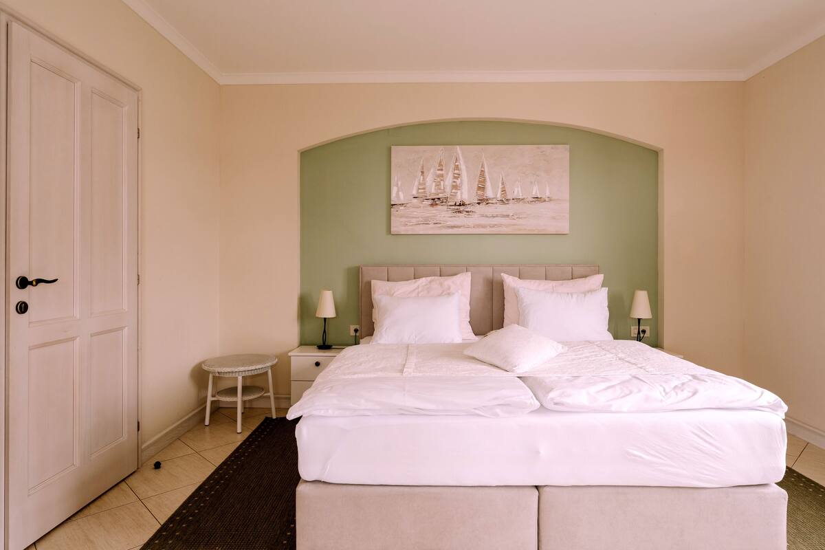 A neatly arranged bedroom with a bed, bedside tables, and a painting on the wall.