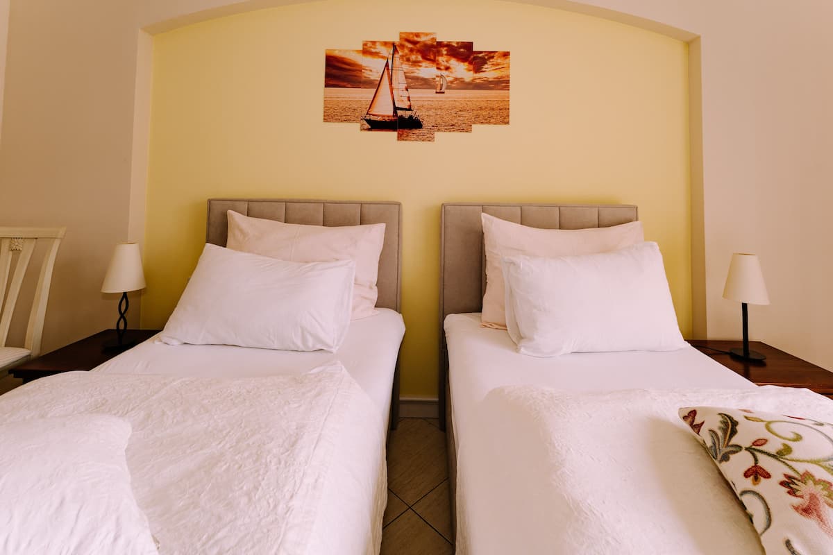 A hotel room with two beds, a wall-mounted painting of a sailboat, and a small table with a lamp.