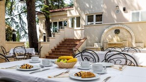 An outdoor dining area with tables set for breakfast, including croissants, bananas, and apples.