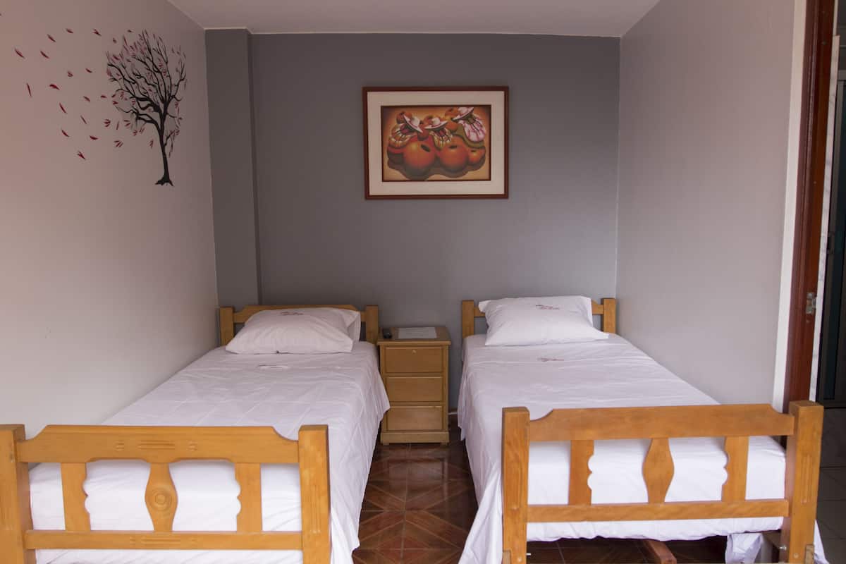 Una habitación con dos camas de madera, una mesita de noche, un cuadro colgado en la pared y un adhesivo mural con la imagen de un árbol con hojas.