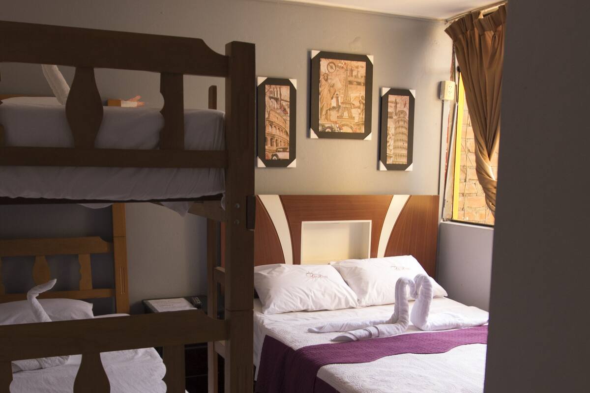 Una habitación de hotel con literas, una cama con colcha morada y cuadros en la pared.