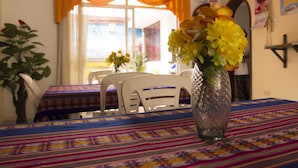 Zona pranzo con tavolo apparecchiato per due, un vaso con fiori gialli e una finestra con tende arancioni.