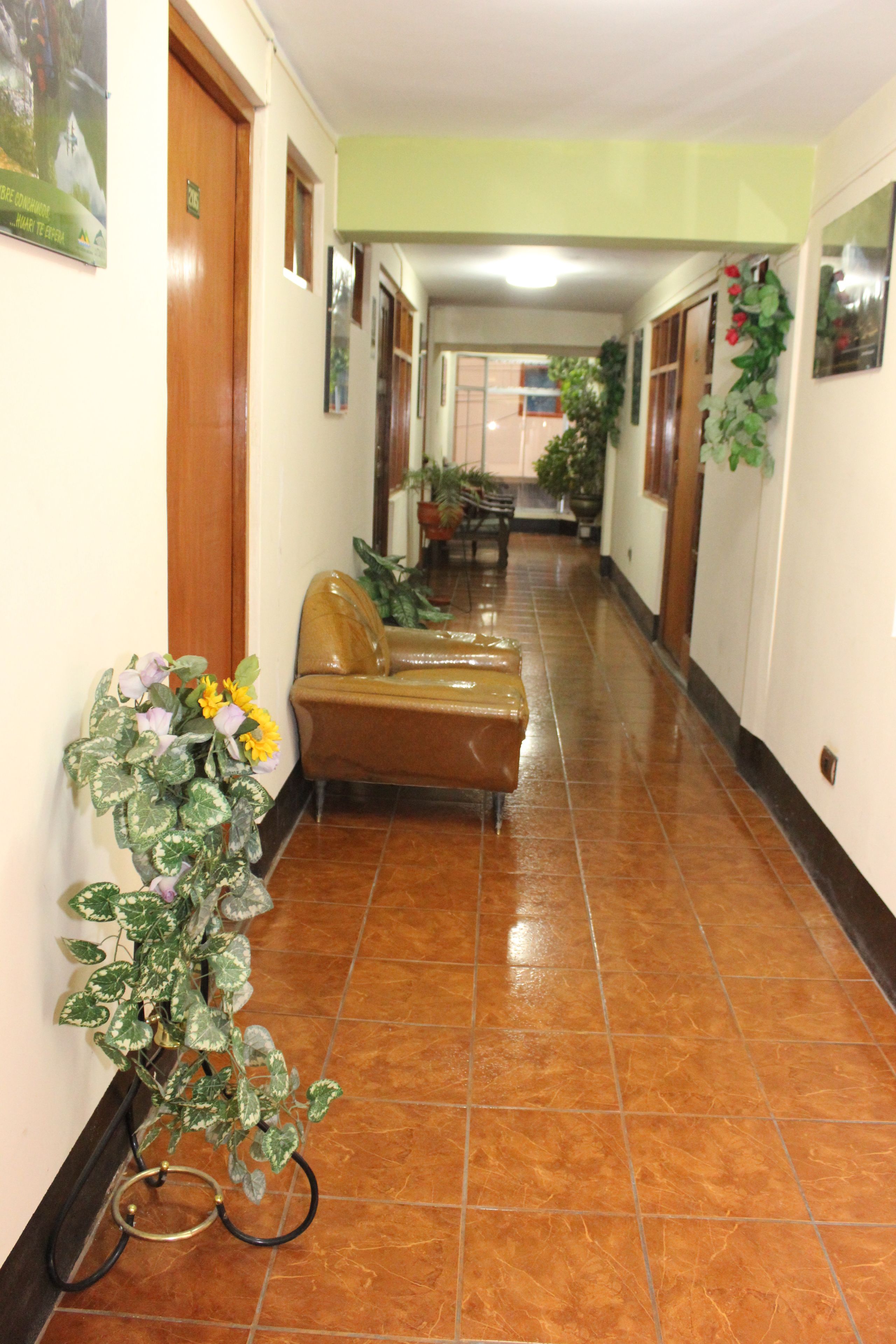 A hotel corridor with a brown leather sofa, potted plants, and a tiled floor.