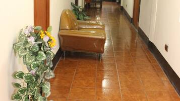 A hotel corridor with a brown leather sofa, potted plants, and a tiled floor.