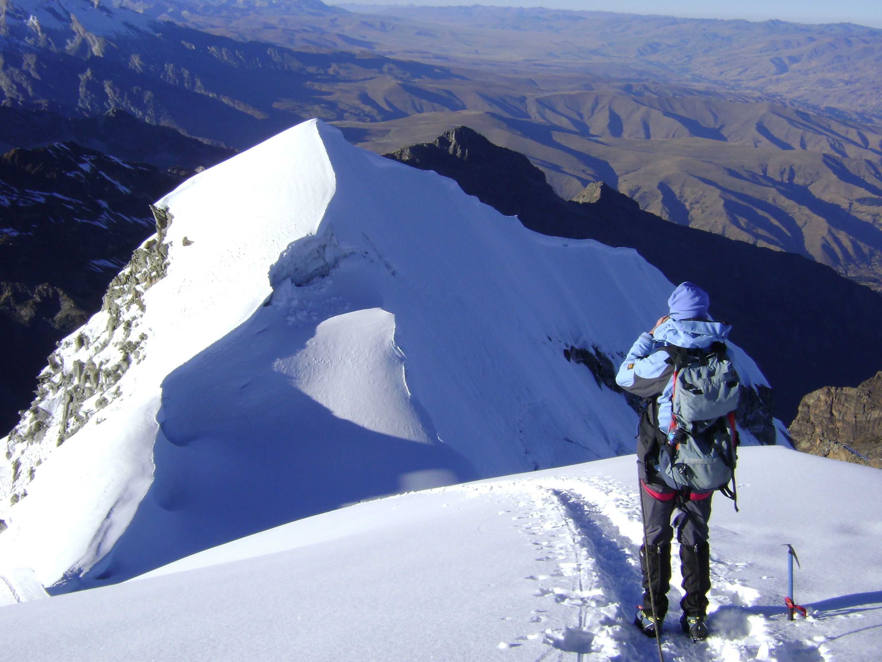 A person standing on a snow-covered mountain peak with a clear view of the surrounding landscape.
