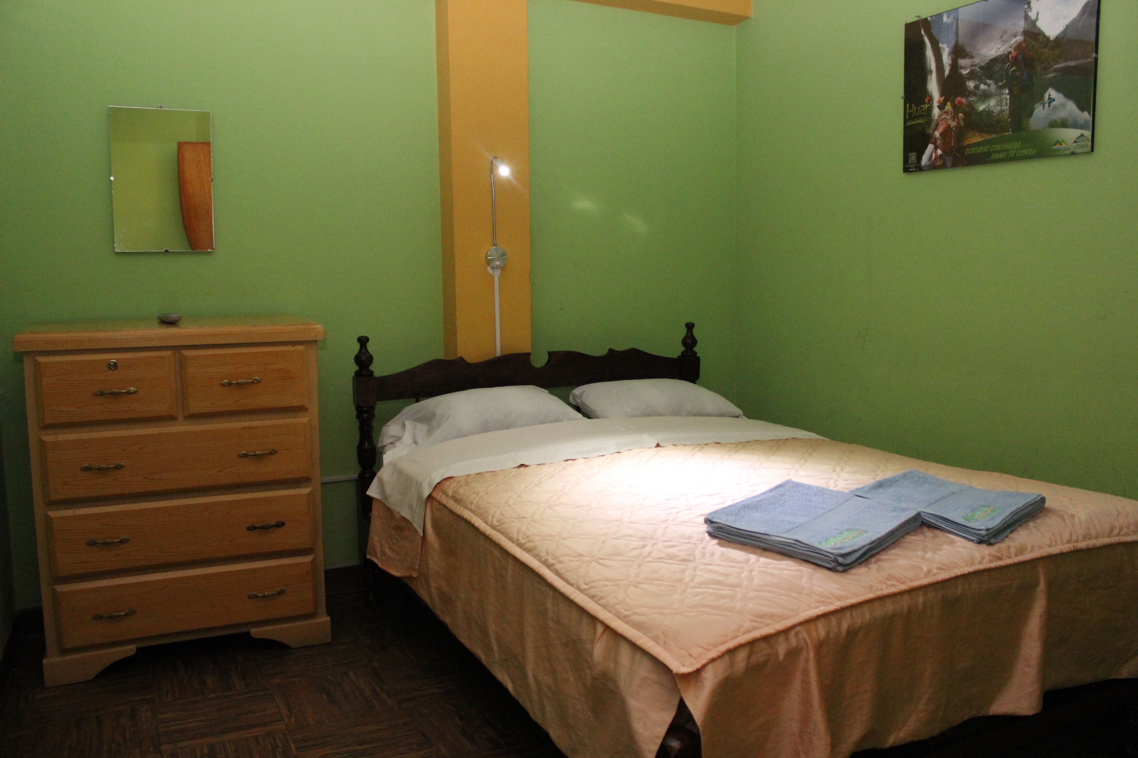 Un dormitorio con cama, cómoda, espejo y lámpara de pared.