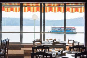 A restaurant with large windows overlooking a lake, featuring wooden chairs and tables. - Hotel Royal (Viverone)